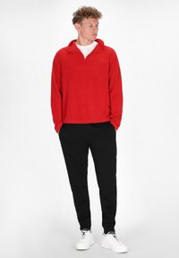 Rød fleece pullover med en kvart lynlås krave, parret med sorte joggerbukser og hvide sneakers, med en afslappet pasform og blød tekstur.
