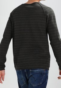 Dunkelgrünes und schwarzes gestreiftes Langarmshirt mit Rundhalsausschnitt, das einen strukturierten Stoff und Raglanärmel aufweist.