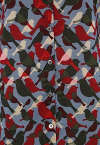 Shirt with blue background featuring an overlapping pattern of red, dark green, and beige bird silhouettes, buttoned with four gray buttons.