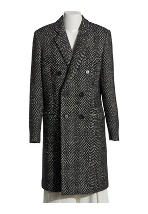 Manteau en laine croisé à motif chevron noir et blanc avec col à revers et poches avant sur un mannequin blanc.