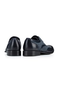 Zapatos de cuero azul oscuro con una parte superior de tela azul texturizada, punta redondeada y tacón negro. Presentan un cordón clásico y elementos de diseño en contraste.