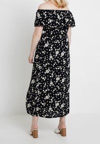 Czarna sukienka maxi w kwiaty z falbanami off-the-shoulder, elastycznym pasem oraz rozsypanymi białymi kwiatami. Masywne sandały na obcasie.