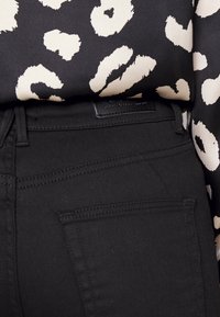 Černé džíny z denimu s přiléhavým střihem, s zadními kapsami a jemnými detaily v prošívání. Nakombinováno s vzorovaným černobílým topem.