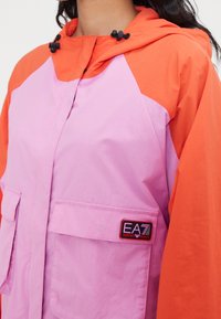 Color-blocked jacket featuring pink and orange panels, two front pockets, a hood with drawstring, and an EA7 logo patch on the chest.