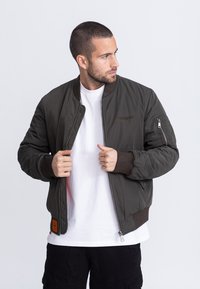 Olivekowa zielona kurtka bomberka z zamkiem błyskawicznym, prążkowanymi mankietami i boczną kieszenią. Posiada pikowaną fakturę oraz haftowane logo na piersi.