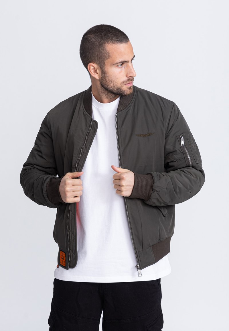 Olivekowa zielona kurtka bomberka z zamkiem błyskawicznym, prążkowanymi mankietami i boczną kieszenią. Posiada pikowaną fakturę oraz haftowane logo na piersi.