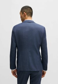 Marineblaues Sakko mit karierter Musterung. Es besitzt einen Schlitz hinten, spitze Revers und kontrastierende Knöpfe an den Manschetten.