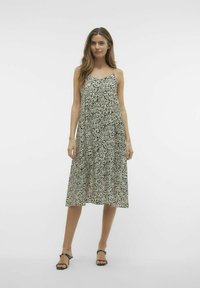 Czarna i biała midi sukienka w wzory z cienkimi ramiączkami, luźnym krojem, dekoltem w serek i zwiewnym materiałem, zestawiona z czarnymi sandałami.