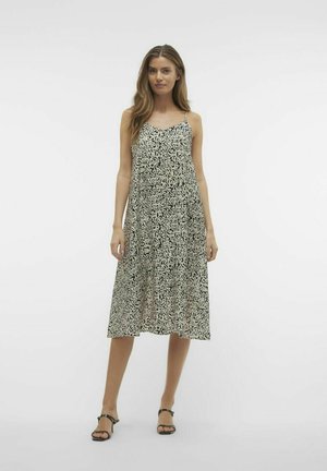 Robe midi à motifs noir et blanc avec des bretelles fines, coupe ample, décolleté en V et tissu fluide, accompagnée de sandales noires.