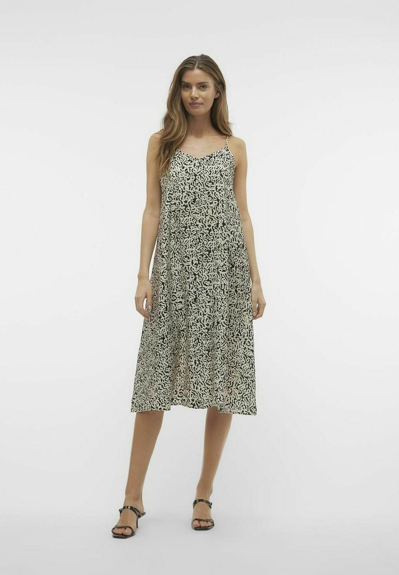 Czarna i biała midi sukienka w wzory z cienkimi ramiączkami, luźnym krojem, dekoltem w serek i zwiewnym materiałem, zestawiona z czarnymi sandałami.