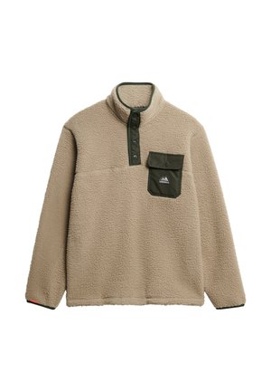 Sudadera de forro polar beige con un cuello alto, tapeta de presión verde y un bolsillo en el pecho. El material tiene un acabado suave y texturizado. Logo de montaña en el bolsillo.