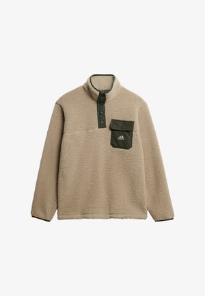 Beige fleecetroyer met hoge kraag, groene drukknoopsluiting en een borstzak. Het materiaal heeft een zachte, textuurachtige afwerking. Berglogo op de zak.