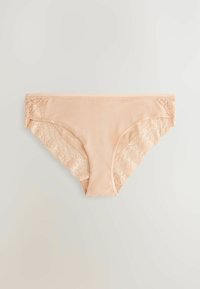 Bežīgu sieviešu bikini stila apakšveļu ar mežģīņu apdari sānos un kāju izgriezumos, izliktu plakani uz neitrāla fona.