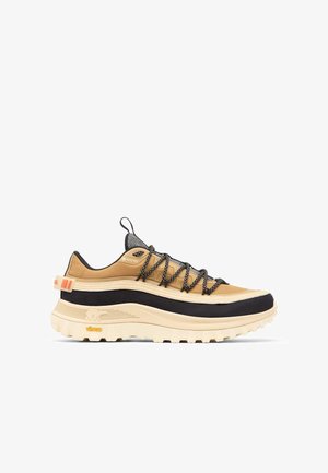 Beige und schwarze Wanderschuhe mit strukturiertem Stoffobermaterial, markantem Schnürsystem und dicker Gummisohle mit tiefen Rillen. Vibram-Logo sichtbar.