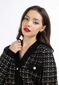 Cardigan nero a maglia con fili dorati, grande colletto e due tasche, ciascuna decorata con bottoni simili a perle. Texture morbida.