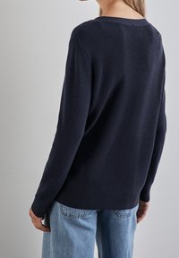 Pull en maille bleu marine avec texture côtelée, col rond large et manches longues, associé à un jean denim bleu clair.