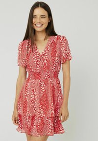 Robe florale rouge avec des manches courtes, décolleté en V, taille élastique et ourlet à volants superposés. Présente des motifs de fleurs blanches sur un tissu texturé.