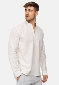 Lightweight linen shirt in off-white, featuring a mandarin collar, long sleeves, and button placket with subtly textured fabric.