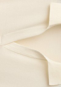 Kremowa tkanina o gładkiej fakturze, z otwartym dekoltem i dwoma nakładającymi się na siebie warstwami materiału u góry.