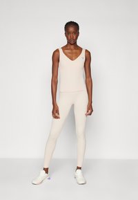 Lys rosa tettsittende tanktop med V-hals og ribbet tekstur, sammen med matchende høytaljede leggings, iført hvite joggesko.