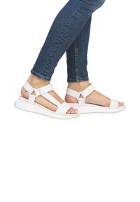 Sandales blanches avec des sangles réglables, une large ouverture pour les orteils et une semelle texturée. Associées à un jean en denim ajusté.