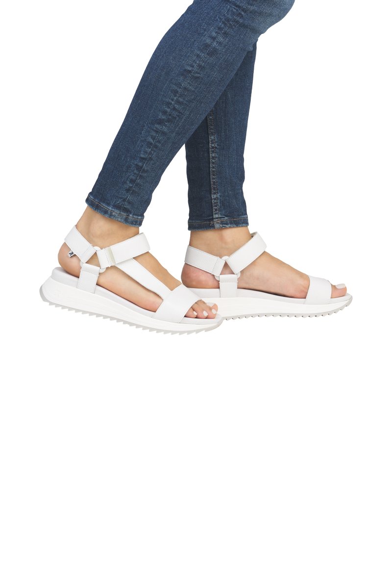 Sandales blanches avec des sangles réglables, une large ouverture pour les orteils et une semelle texturée. Associées à un jean en denim ajusté.