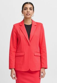 Koraalblazer met een enkele knoopsluiting, twee voorzakken en ingeknipte revers. De stof oogt soepel, ontworpen voor een getailleerde silhouet.