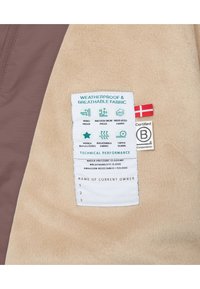 Beżowa tkanina polarowa z brązowymi akcentami. Metka z instrukcją pielęgnacji szczegółowo opisująca cechy wodoodporne, w tym odporność na wodę i śnieg, uszczelnione szwy oraz oddychalność.