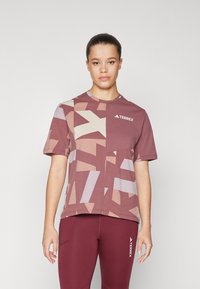 Trumpo rankovėmis maroon sportinis marškinėliai su geometriniu raštu šviesiai bežinių ir levandų spalvų. Turi apvalią iškirptę ir logotipą ant krūtinės.