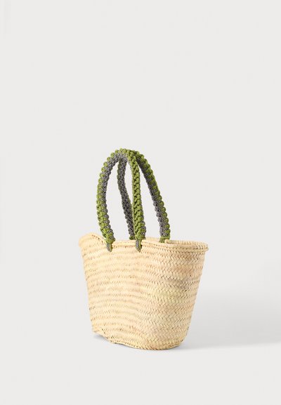 Sac cabas en paille tissée avec deux grosses poignées tressées vertes et noires, debout sur un fond uni et clair.