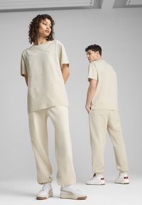 Light beige cotton T-shirt and matching pants. The apparel features a relaxed fit, smooth texture, and a minimal logo. White and beige shoes are paired.