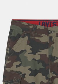 Zbliżenie na spodnie cargo w kamuflażowym wzorze z boczną kieszenią, szlufkami na pasek, zapięciem na guzik oraz czerwoną górą z logo Levi's.