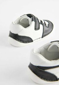 Černobílé dětské boty z kůže, s páskem na suchý zip, kulatou špičkou a kontrastním prošíváním.