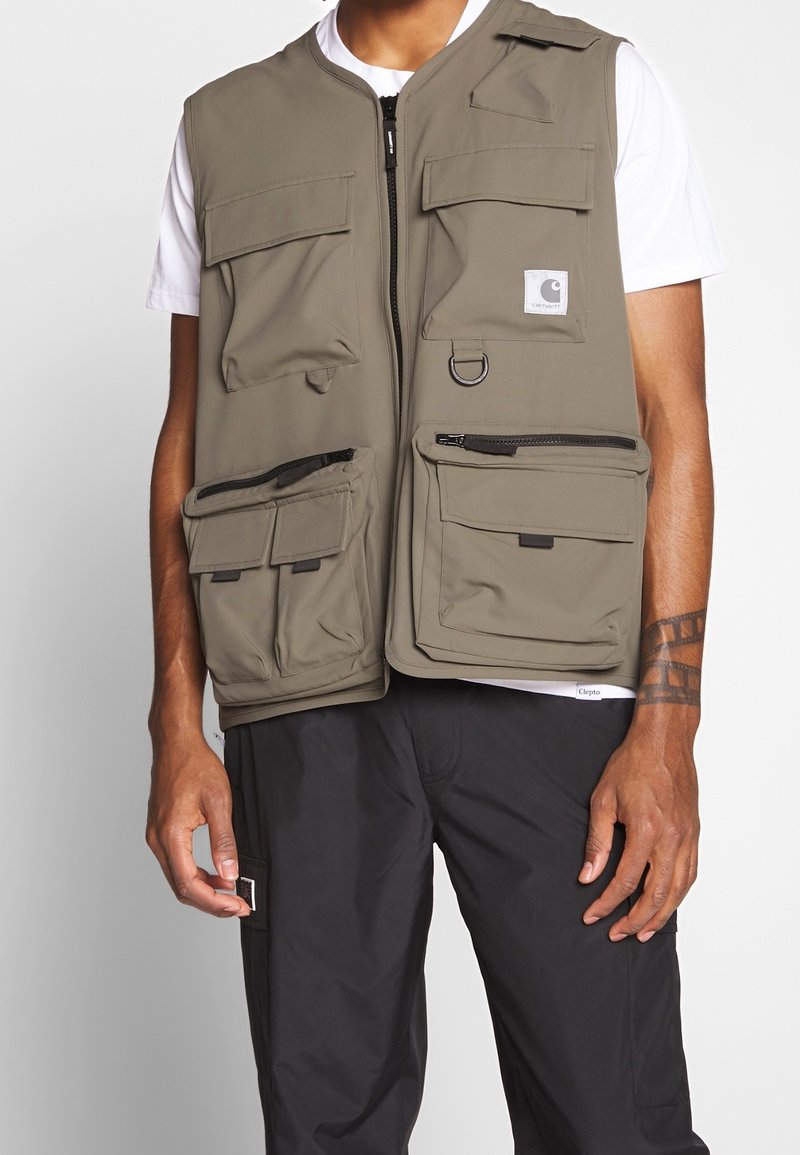 Khaki nytta väst med flera fickor, dragkedjor och detalj i form av en ring. Tillverkad i slitstarkt tyg; har dragkedja fram och en avslappnad passform.