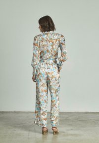 Jumpsuit con stampa floreale in tessuto leggero, con maniche lunghe, vita elastica e vestibilità rilassata. Colori morbidi di blu, marrone e crema.