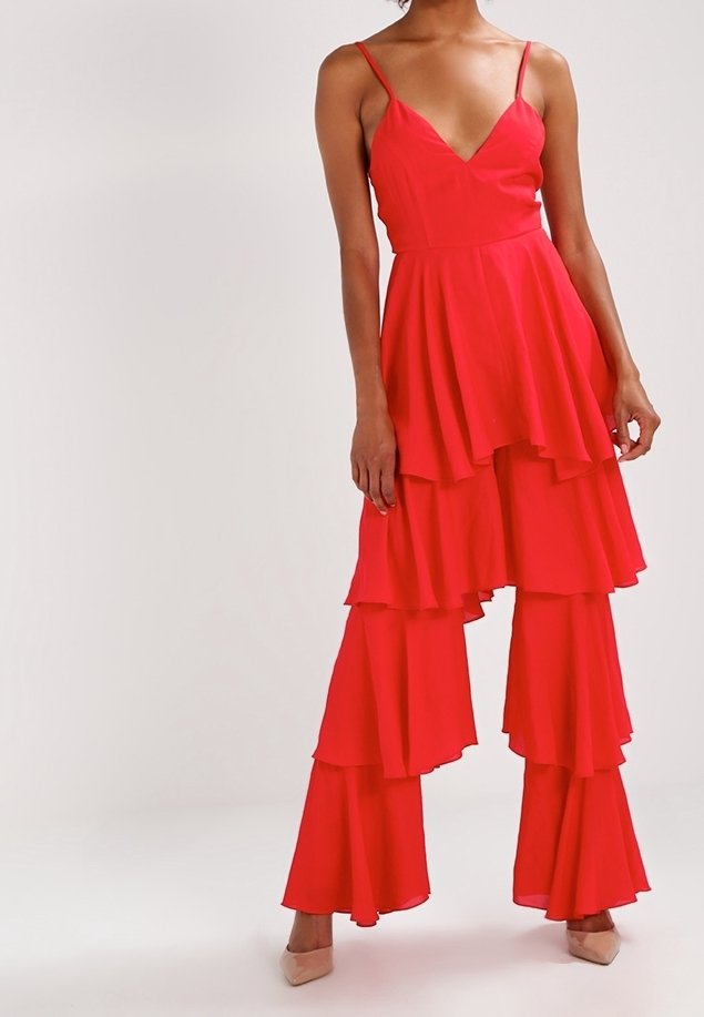 Personne portant une robe superposée rouge vif avec de fines bretelles et des volants évasés sur un pantalon large assorti et des talons beige.