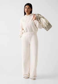 Souprava pohodlného oblečení ve smetanové barvě, která obsahuje mikinu s kapucí a široké kalhoty. Měkká látka s vyšívaným logem.