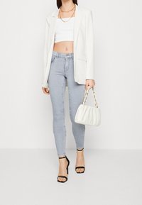 Blazer blanco con rayas, top corto blanco, jeans ajustados azul claro, tacones negros con tiras y un bolso acolchado blanco con herrajes dorados.