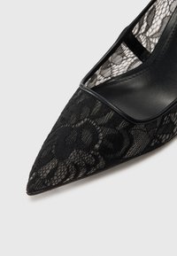 Pantofi cu tocul negru din dantelă, cu vârful ascuțit, având un superior din dantelă transparentă și accente solide din piele neagră de-a lungul marginii. Model floral texturat.