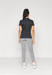 Μαύρη πόλο μπλούζα και γκρίζα στενά παντελόνια. Η μπλούζα διαθέτει γιακά και κοντά μανίκια, ενώ το σύνολο συνδυάζεται με άσπρα παπούτσια.