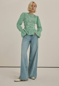 Grøn gingham bluse med puffærmer og peplum talje, parret med lyseblå brede bukser og cremefarvede spidse sko.