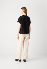 Haut noir à manches courtes avec une coupe décontractée, associé à un pantalon large crème. Texture lisse, design minimaliste et sans motifs ni ornements visibles.