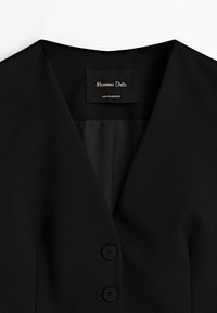 Blazer noir sur mesure avec un col en V, deux boutons noirs et une étiquette indiquant "Massimo Dutti Fabriqué au Maroc".