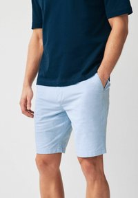 Helle blaue Baumwollshorts mit einem schlichten Design, ausgestattet mit Seitentaschen und einer glatten Textur. Kombiniert mit einem marineblauen T-Shirt.