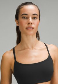 Crni sportski bralet sa tankim trakama, glatkom teksturom, prilagođenim dizajnom i pravokutnim izrezom, nosi ga model na sivoj pozadini.