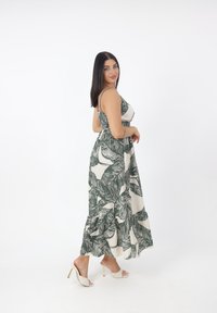 Maxi abito in crema con stampa di foglie verde scuro, dotato di spalline sottili, vita elasticizzata e orlo fluido con volant.