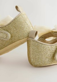 Goldglitzer-Ballettschuhe mit abgerundeter Spitze, einem Stoffbogen und beigen Riemen, die eine strukturierte Sohle und ein weiches Innenfutter aufweisen.