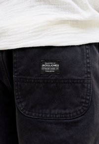 Τσέπη σε μαύρο παντελόνι με υφασμάτινη ετικέτα που γράφει «Jack & Jones Cotton Dry Goods Div. Established 1990» κάτω από λευκό υφασμάτινο ύφασμα.