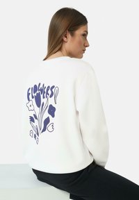 Lichtcrème sweatshirt met ronde hals en lange mouwen, voorzien van een marineblauw bloemenpatroon op de rug. Zachte textuur en een comfortabele pasvorm.