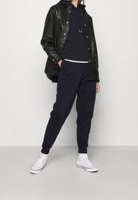 Czarna skórzana kurtka nałożona na granatową bluzę z kapturem i granatowe spodnie dresowe, zestawiona z białymi wysokimi trampkami. Prosty krój o luźnym fasonie.